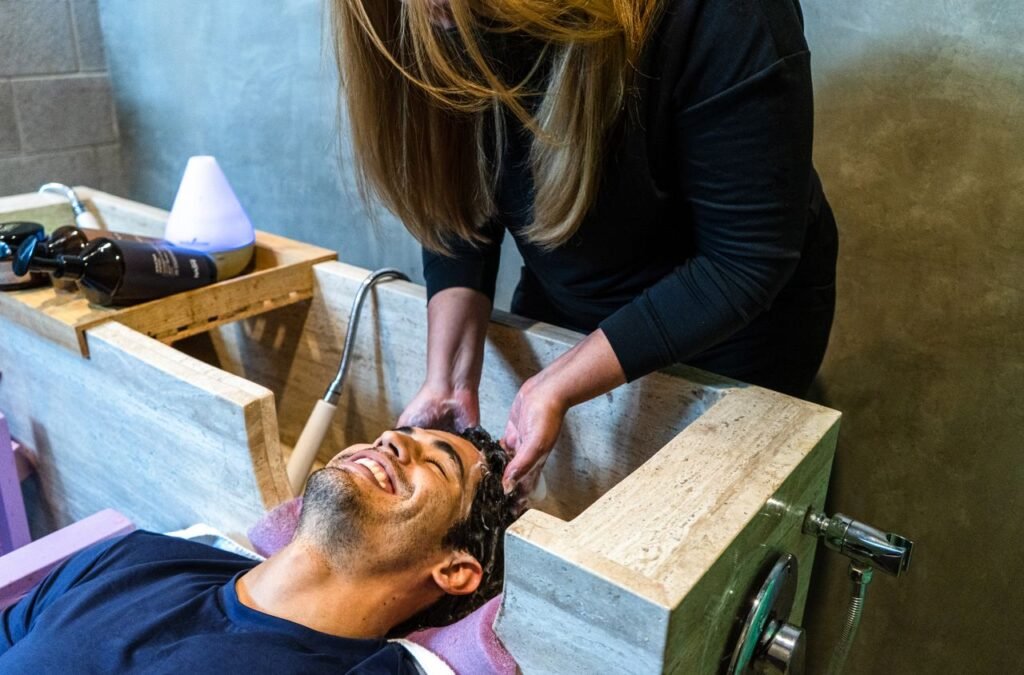 A man smiles while getting his hair washed by a hairdresser in a modern salon setting.