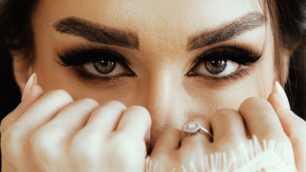 Intense close-up photography of a woman's eyes with striking makeup and elegant ring.